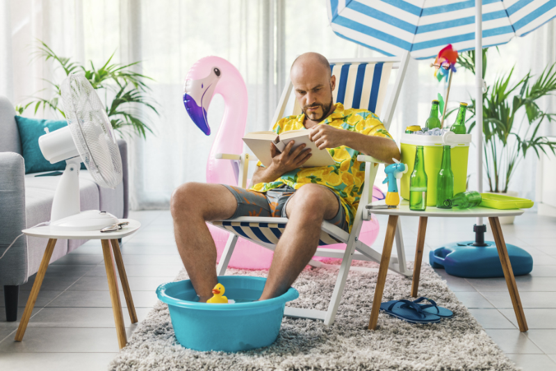 Prepare for Hot Weather With an Air Conditioning Tune-up. Man spending his summer vacations at home, he is sitting on a deckchair in the living room and reading a book.
